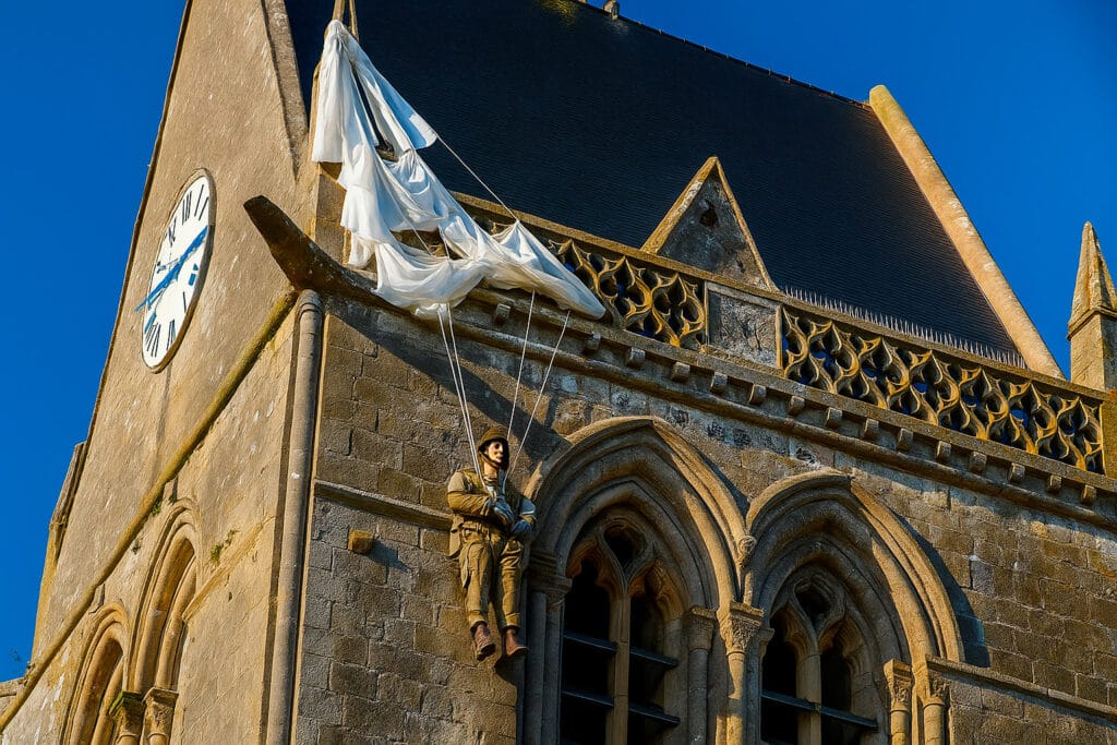 Manequim do paraquedista John Steele pendurado com seu paraquedas na torre da igreja de Sainte-Mère-Église, na Normandia.